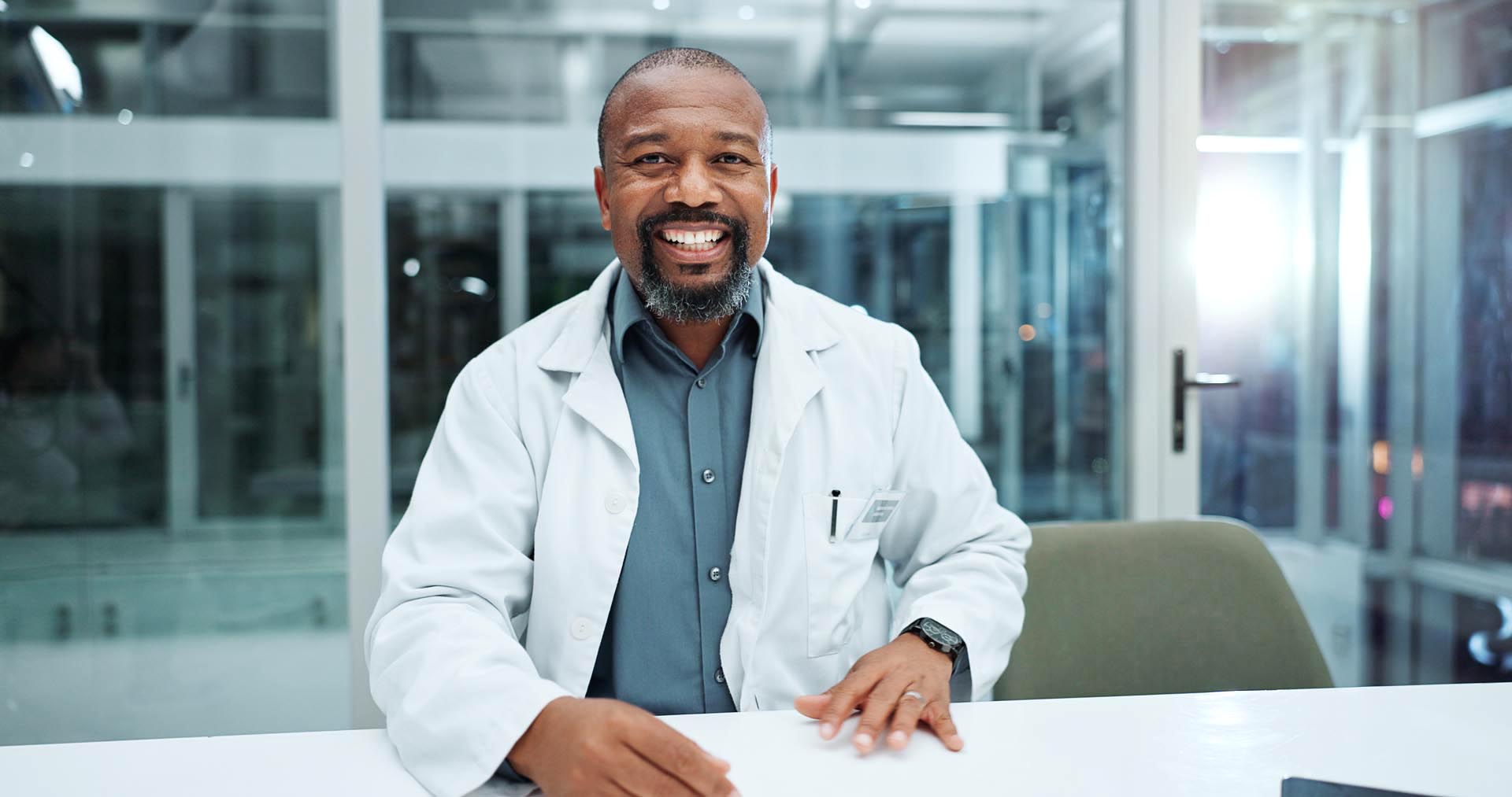 Happy male doctor sitting at his desk in his hospital office