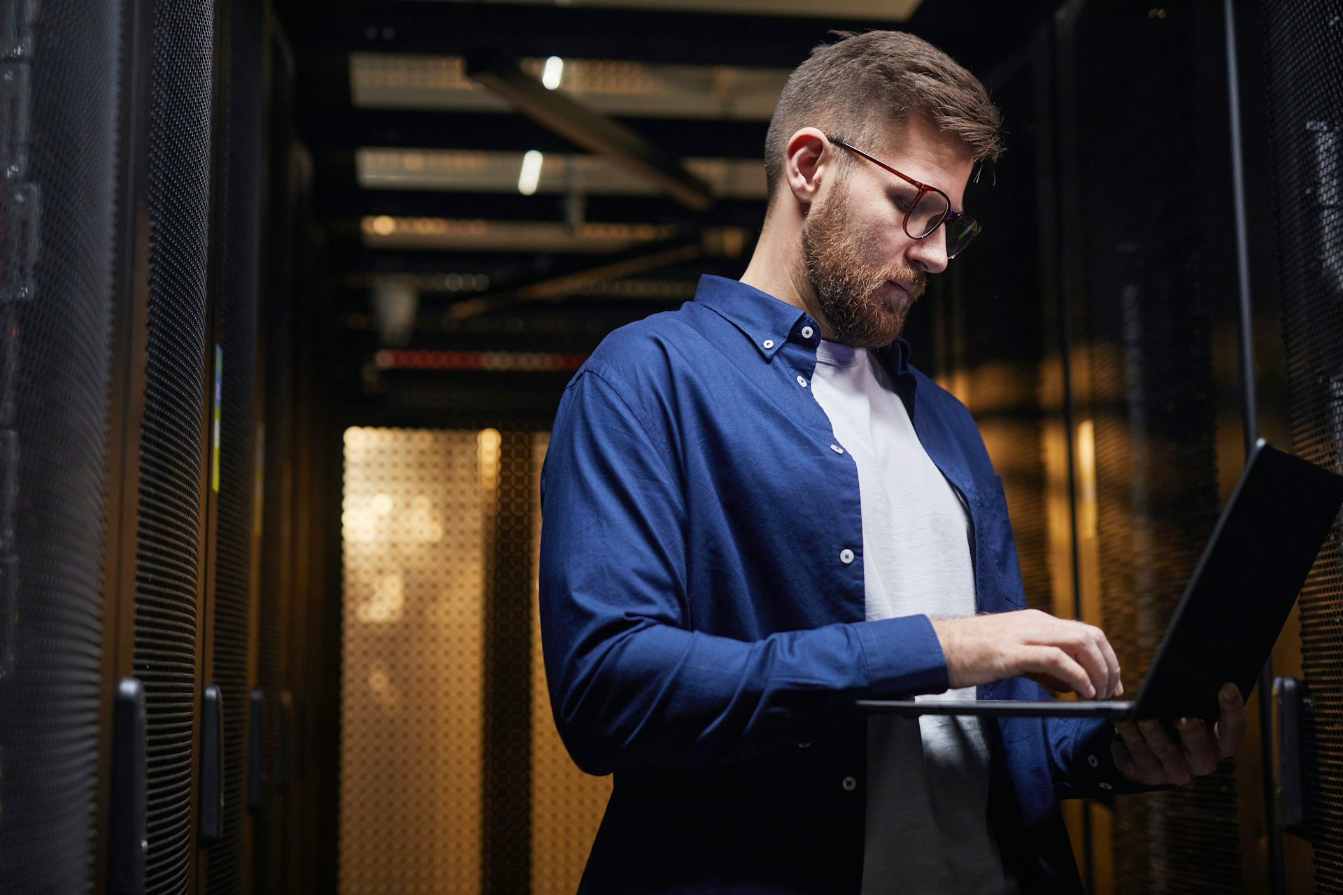 Man standing near servers working on his laptop on Healthcare IT Security